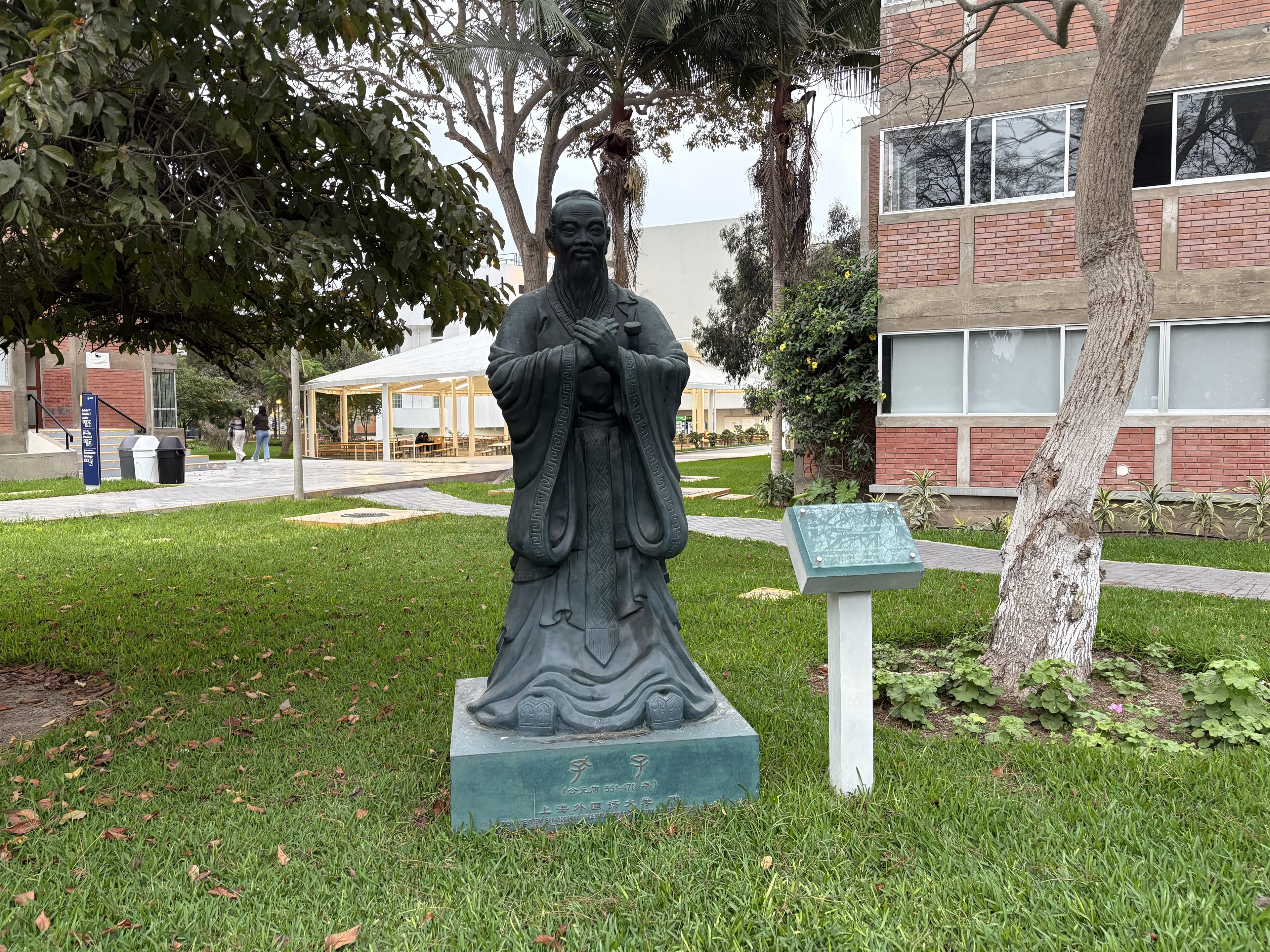 Estatua de bronce de Confucio sobre un pedestal, en un jardín del campus de la PUCP
