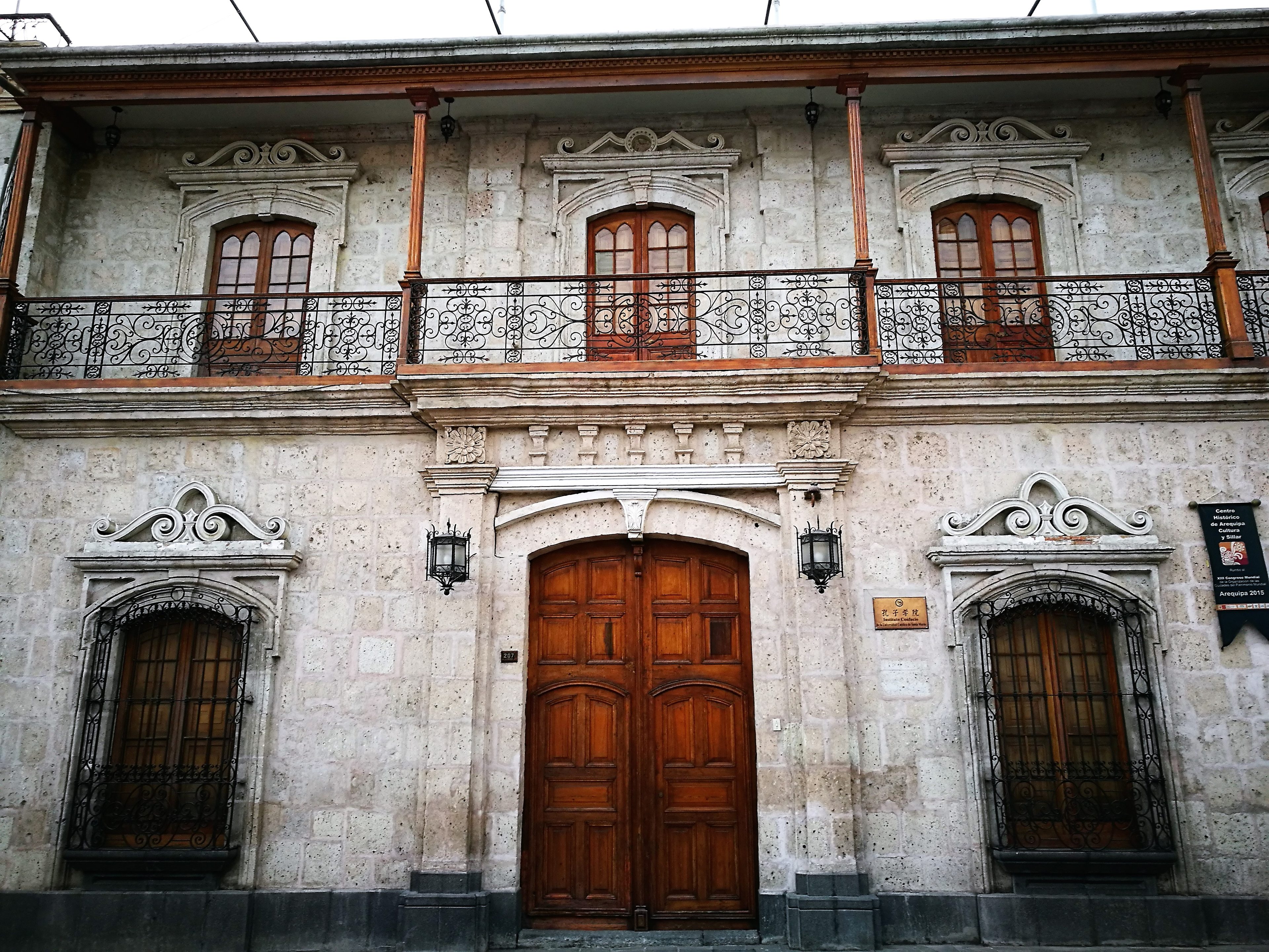Fachada de sillar con balcón de madera y una placa del Instituto Confucio junto a la puerta