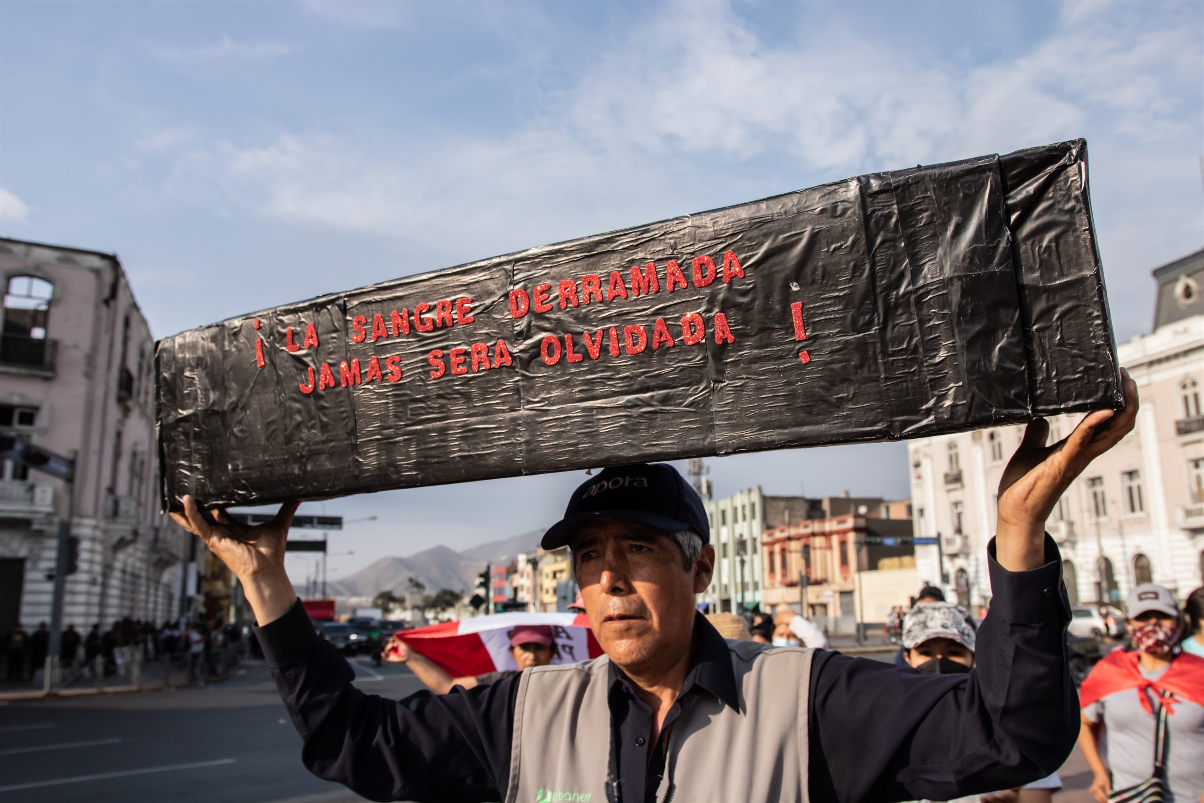Un manifestante sostiene sobre su cabeza un ataúd simbólico con la frase «La sangre derramada jamás será olvidada»